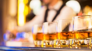 Four small glasses of whisky are placed on a bar top